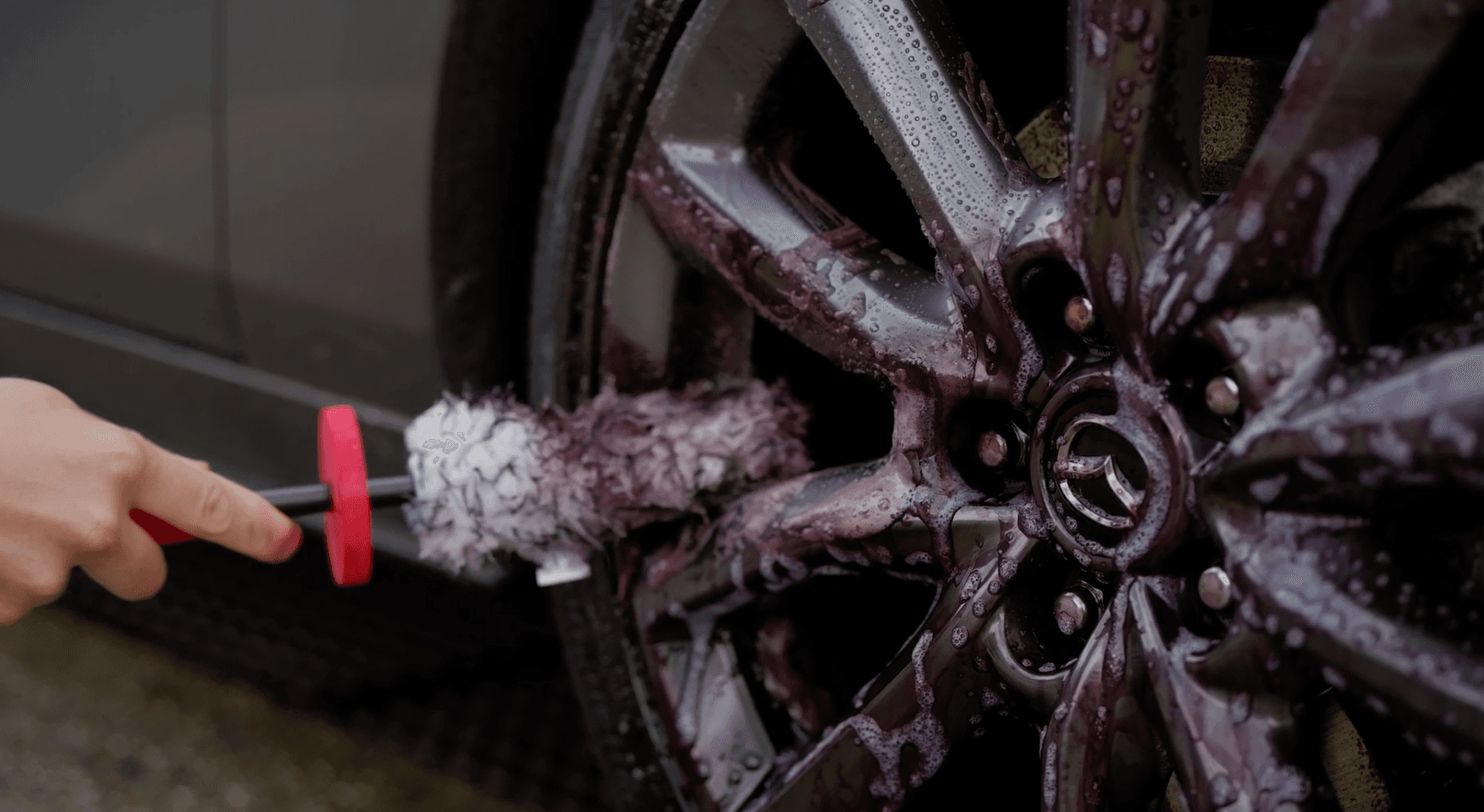 Wheel of a Mazda being cleaned with a wheel brush and wheel cleaner.